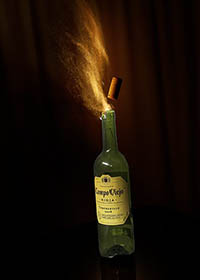 photograph of a bottle of wine with the cork exploding from the mouth