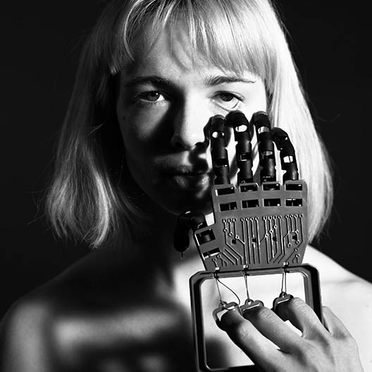 black and white photograph showing a woman holding a mechanical hand to her face