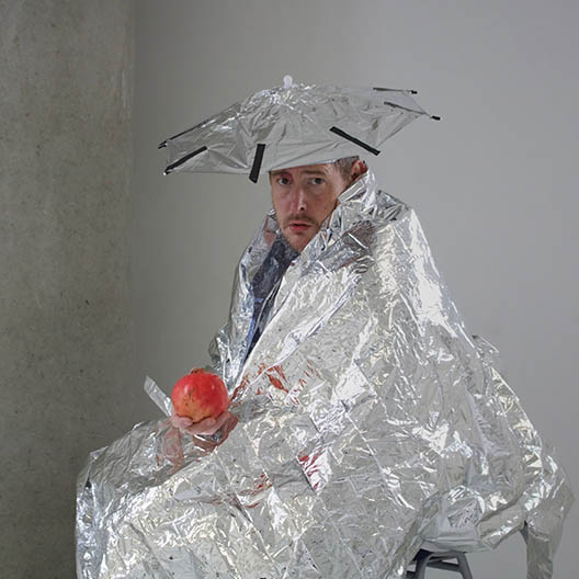 photograph of a man wrapped in tin foil holding a pomegranate