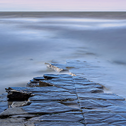 Photograph of a stone path leading out into the sea, semi-submerged.