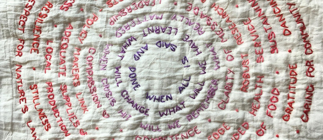 Words stitched into fabric in a circular motif. The text in the centre is purple and changes colour as it reaches the edge, fading through pinks to red.