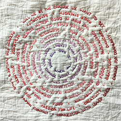 Words stitched into fabric in a circular motif. The text in the centre is purple and changes colour as it reaches the edge, fading through pinks to red.